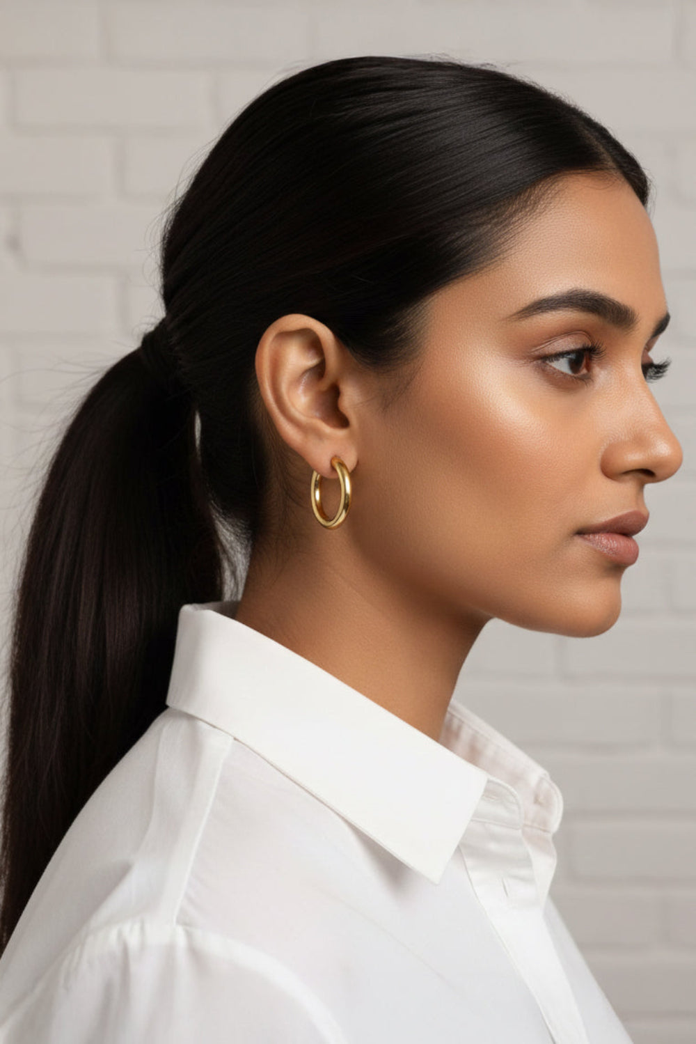 Woman with a ponytail wearing gold hoop earring against a neutral background